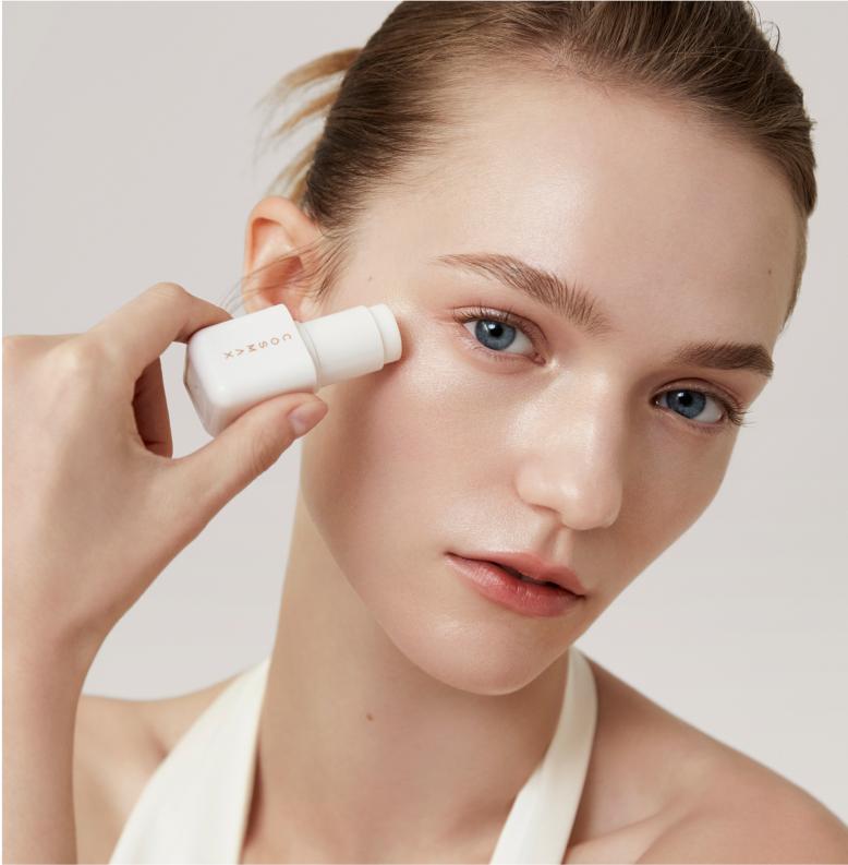 Model tilting head holding COSMAX stick balm near eye