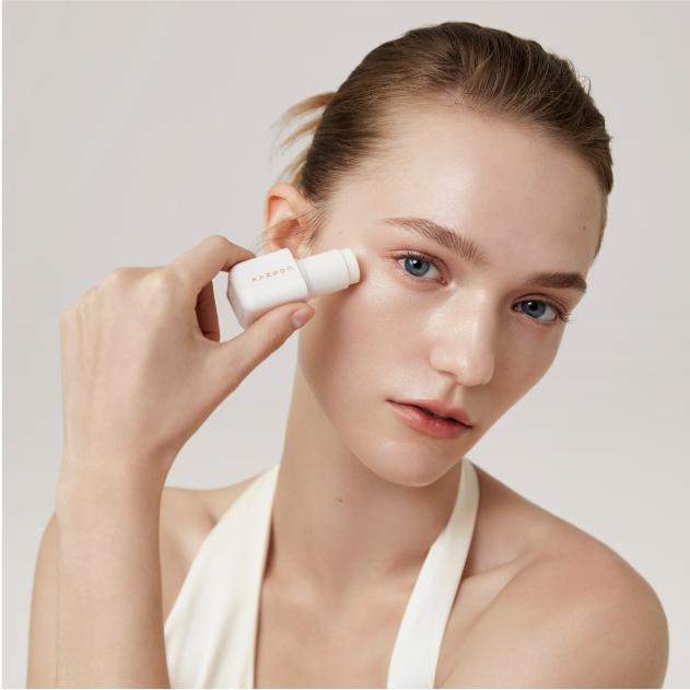 Model tilting head holding COSMAX stick balm near eye