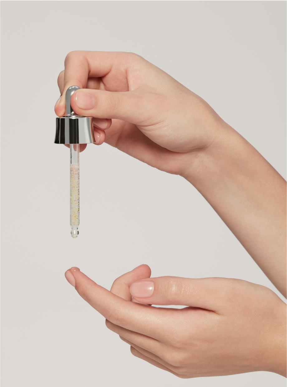Close-up of model’s hands holding a dropper tip containing ampoule in one hand and testing the product with the fingertip of the other hand