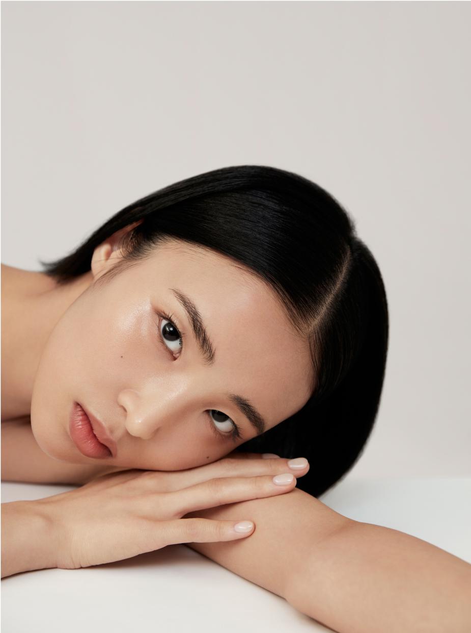 Model lying on side with head resting on one arm and hand holding the other arm, gazing directly at the camera